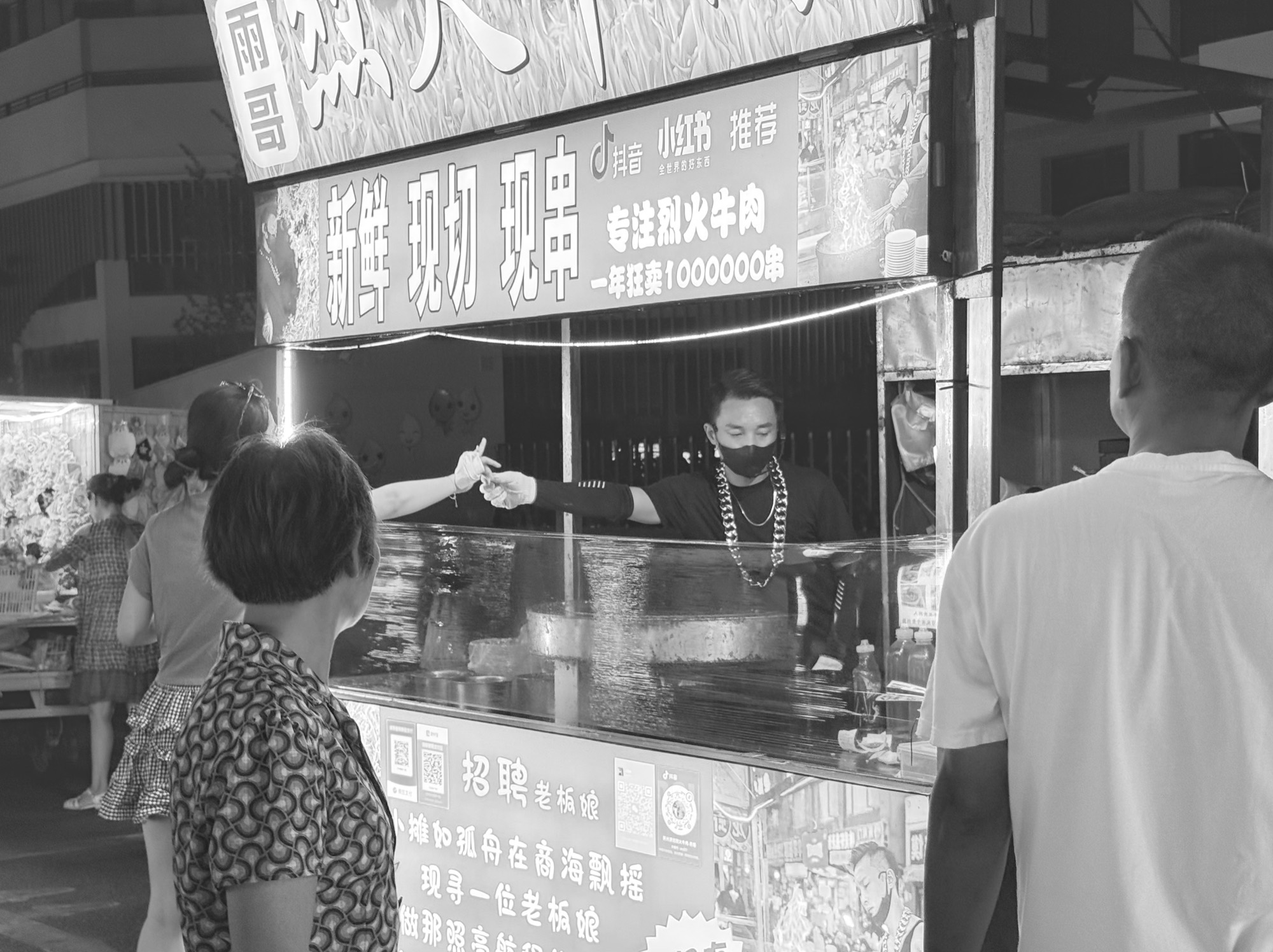 黑白夜市摊前，戴口罩的摊主隔着柜台向顾客递出食物